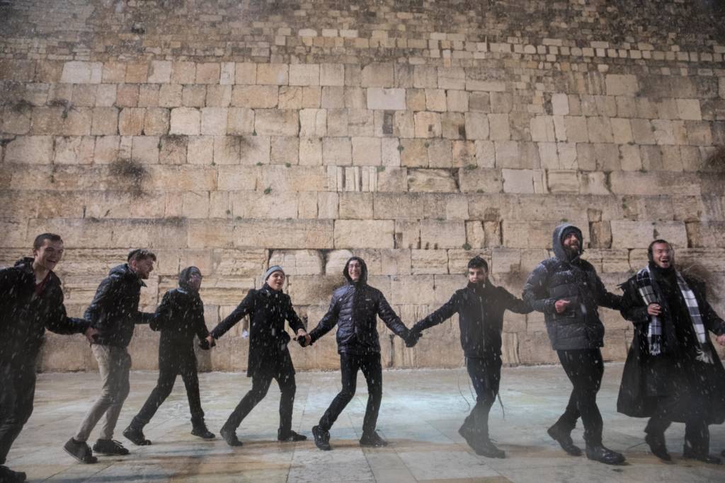 Men dance in the snow at the Western Wal, in Jerusalem. (Noam Rivkin Fenton/Flash90)