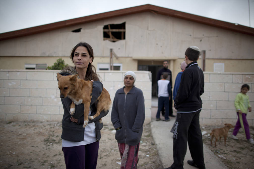 Israelis next to a house damaged by Palestinian rocket during a previous attack. (AP Photo/Oded Balilty)